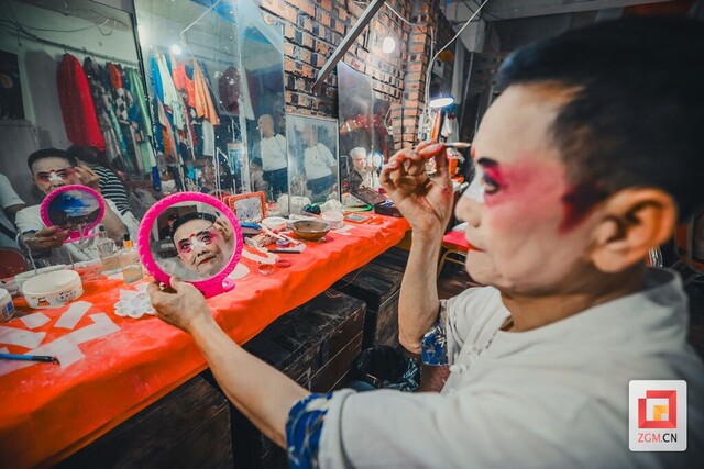 演员正对着一面布满水渍的旧镜子，手握画笔，正精心勾勒脸谱上的线条 记者 宋姿熠 摄.jpg